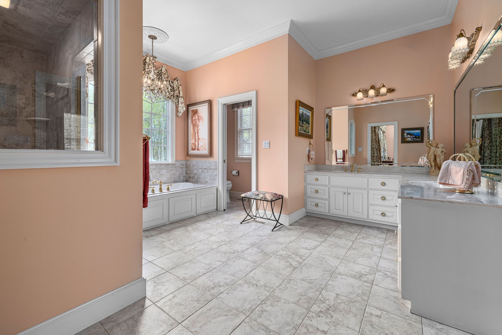 Spacious bathroom in peach tones featuring white cabinets and elegant decor.